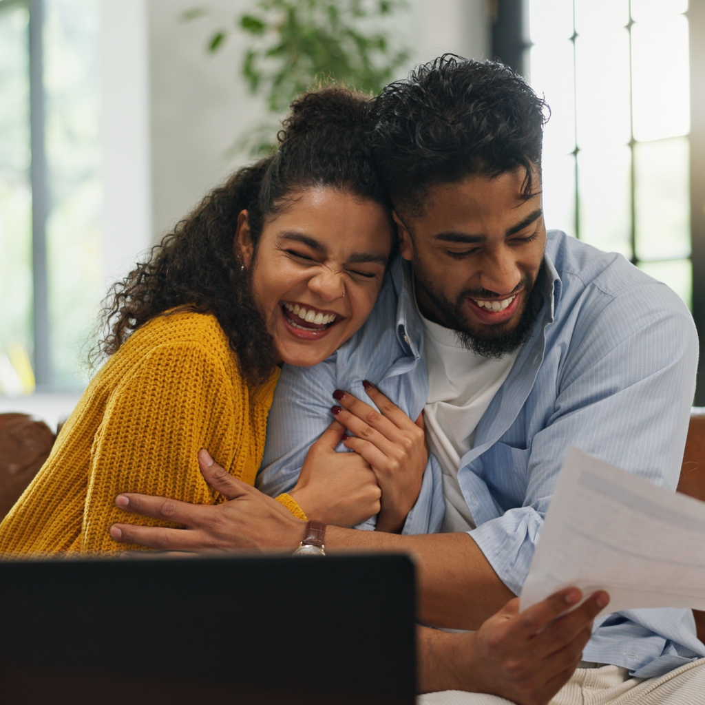 Man and woman hugging with laptop and paper in front of them.