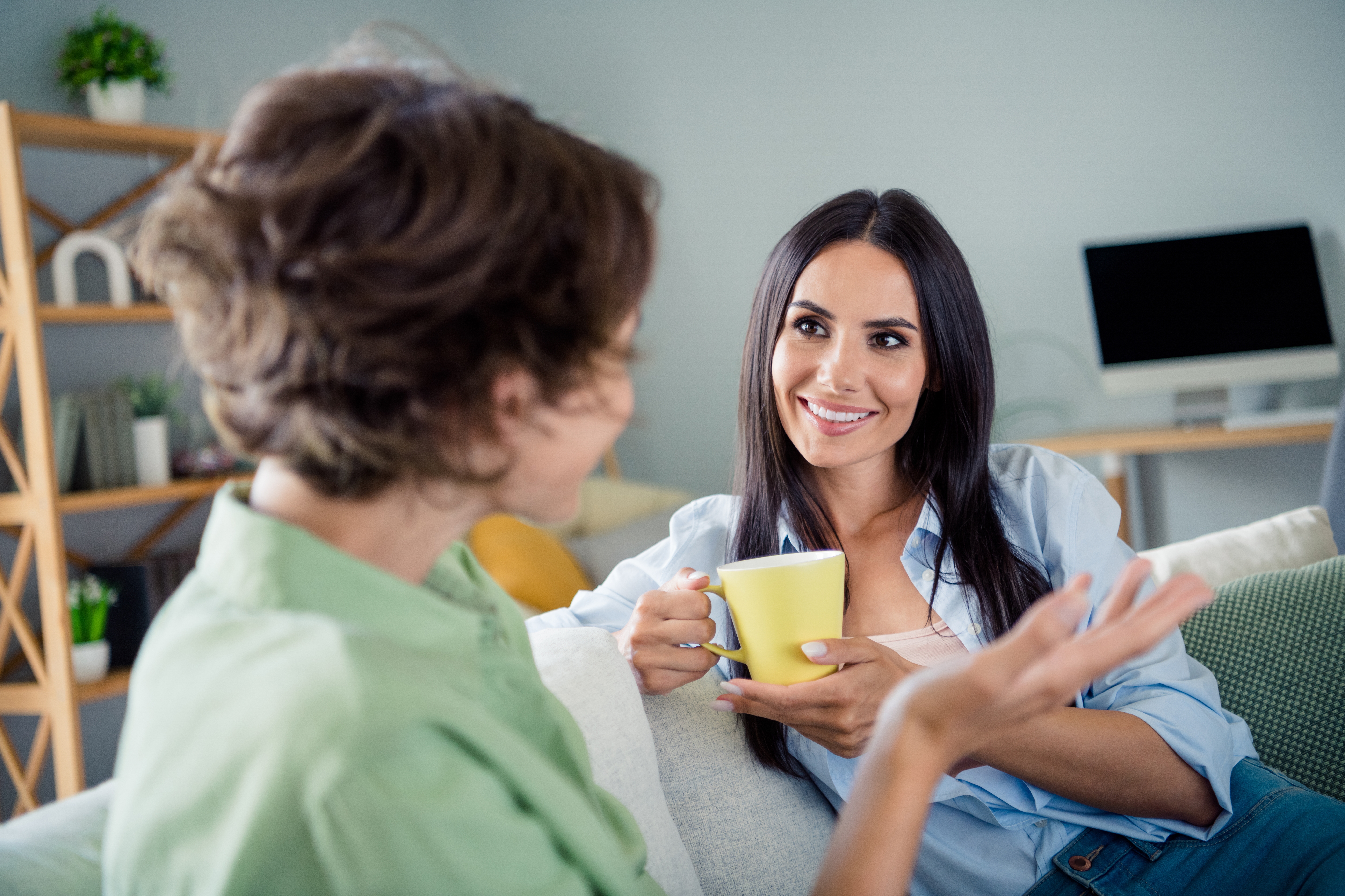 Two friends sitting on the couch, talking and drinking tea.